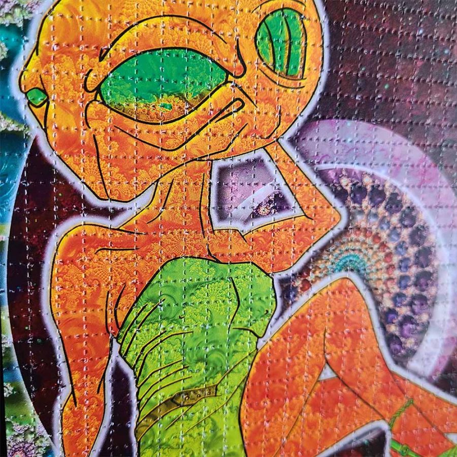 Close up photo of LSD Blotter acid art featuring a green eyed orange alien