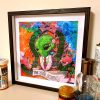 photo of a framed lsd blotter acid art print featuring psychedelic colours and an alien wearing a suit with pierced eyebrow surrounded by space bugs with a scroll that says tame your demons