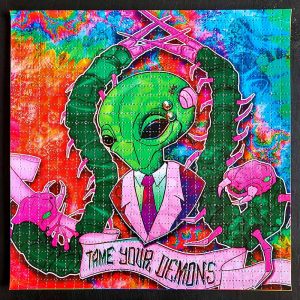 photo of a lsd blotter acid art print featuring psychedelic colours and an alien wearing a suit with pierced eyebrow surrounded by space bugs with a scroll that says tame your demons