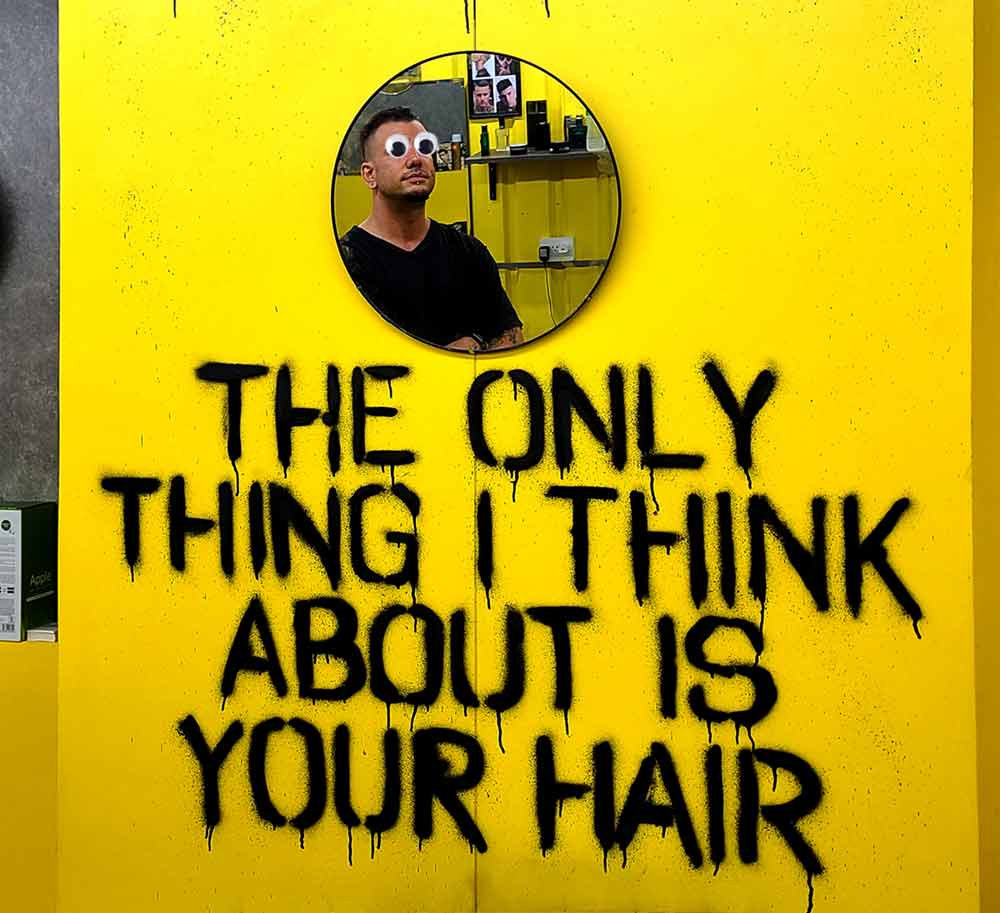 stencil style freehand lettering graffiti mural on bright yellow wall at The Ambassador Barbershop, Bangkok by artist Vinni Kiniki