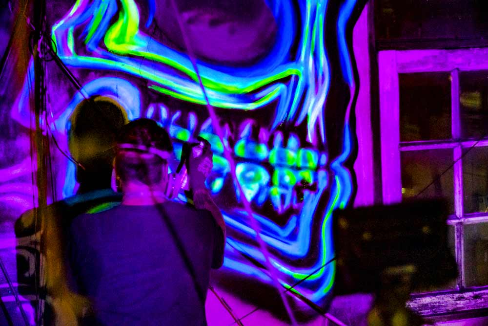 close up of black light street art painting by vinni kinki - flourescent x-ray skull teeth
