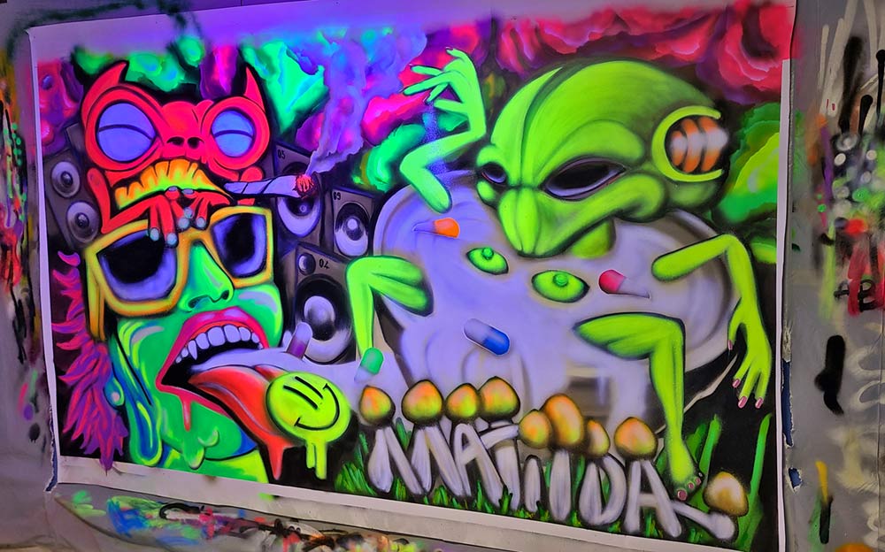 Psychedelic-themed black light graffiti canvas commissioned for a festival birthday party, featuring alien and trippy characters neon elements that glow under UV light