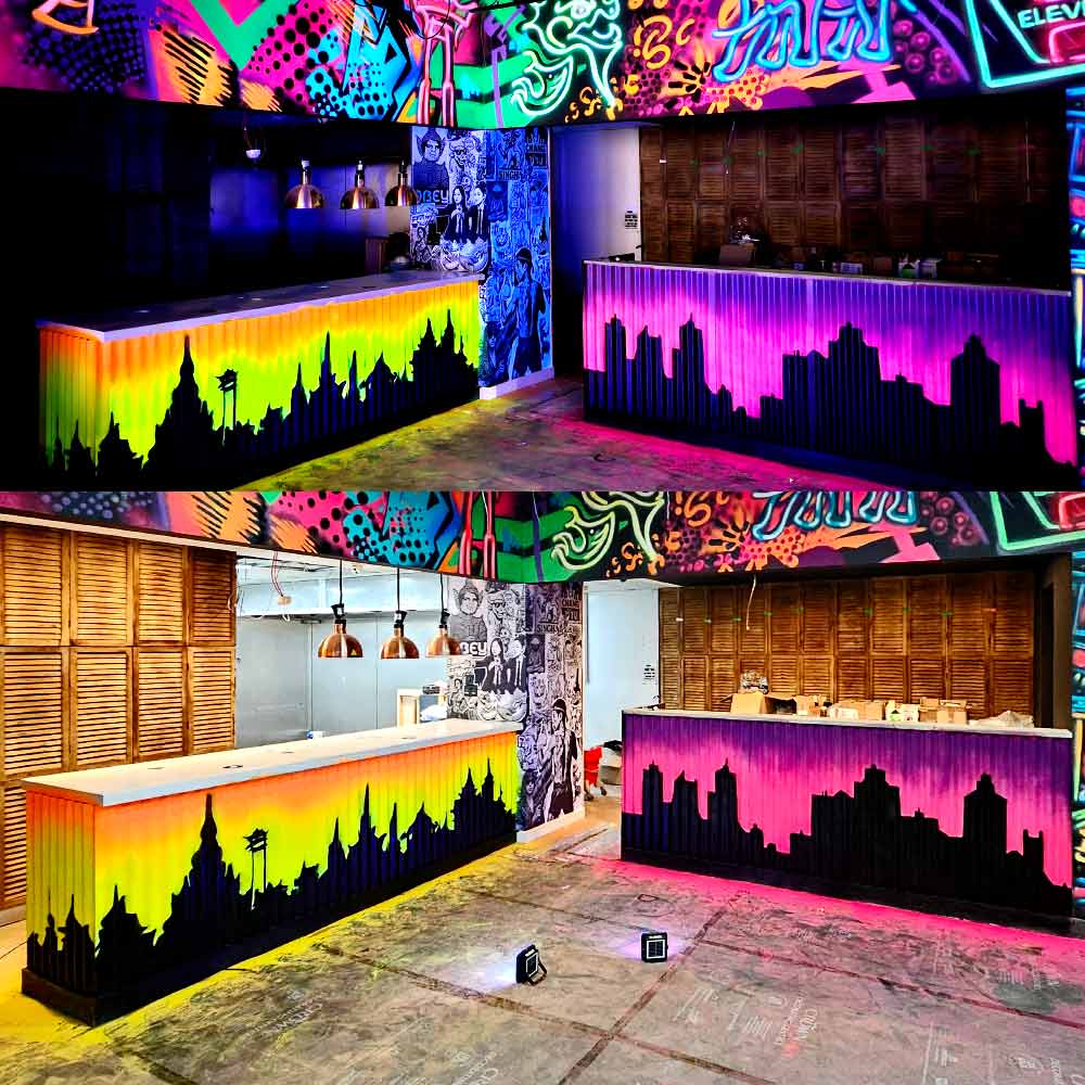 UV reactive black light mural on corrugated metal bar and kitchen counter at My Thai restaurant in Manchester Piccadilly, featuring a neon glowing cityscape silhouette of old and new Bangkok by artist ViNNi KiNiKi