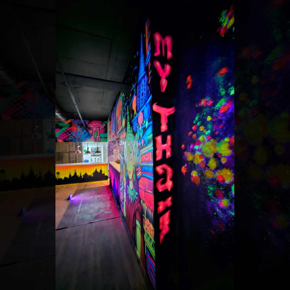 Vertical UV reactive mural in hidden wall gap spelling ‘My Thai’ in fiery textured red letters, painted by artist ViNNi KiNiKi at Manchester Piccadilly restaurant