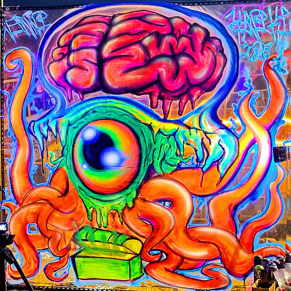 UV-reactive street art mural on translucent canvas by ViNNi KiNiKi, painted at Bangkok Island Event for Galleries Nights; features a vivid surreal jellyfish creature with a large glowing eye, orange tentacles, and an exposed pink brain floating above, painted using fluorescent neon spray paint colours. 