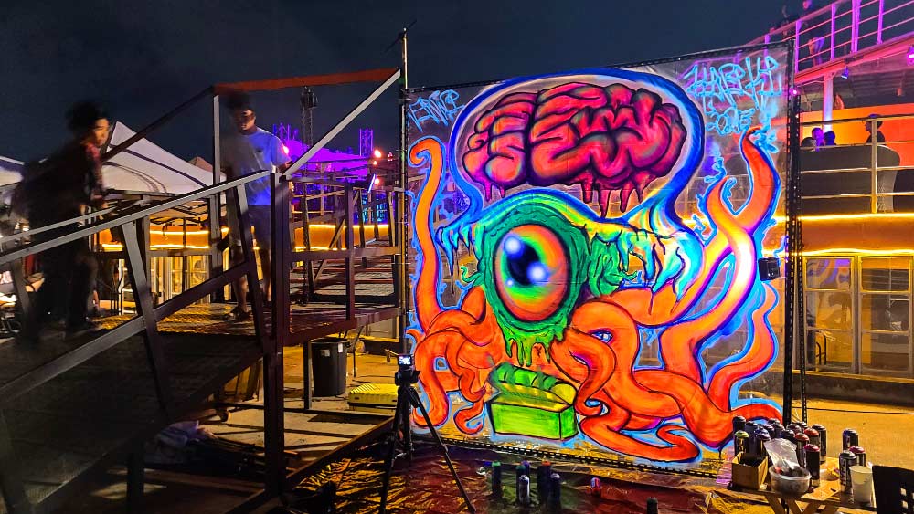 Black light graffiti mural of a psychedelic jellyfish sea monster by ViNNi KiNiKi, painted live on Bangkok Island during Galleries’ Nights Bangkok 2025