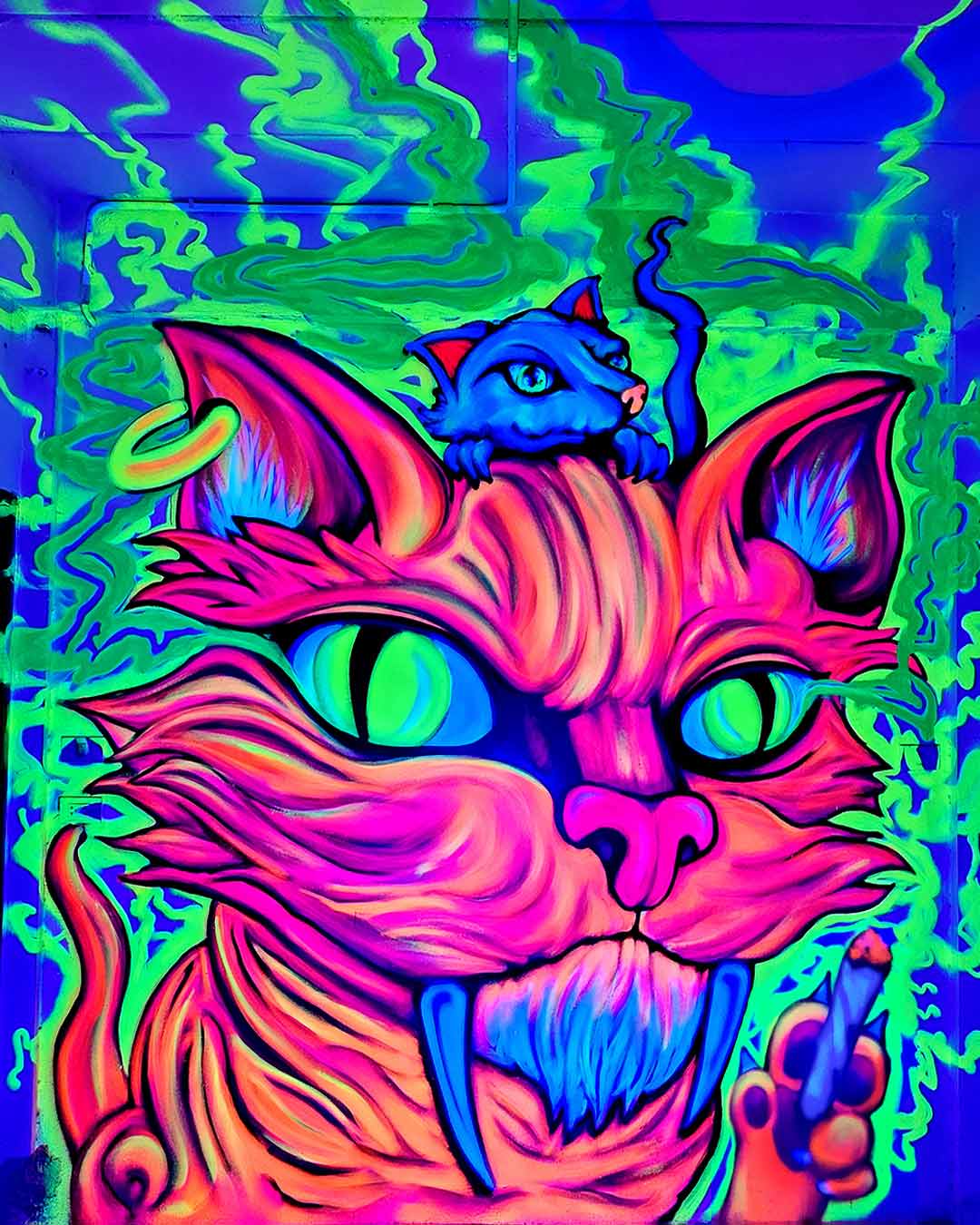 Psychedelic UV black light street art mural by Vinni Kiniki featuring a fluorescent neon pink smoking cat with glowing green eyes, a smaller blue rat on its head, and ultraviolet reactive green smoke painted with aerosol spray paint.